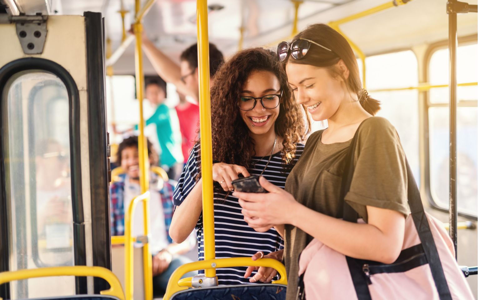 Two friends laughing and watching phone while waiting for bus to